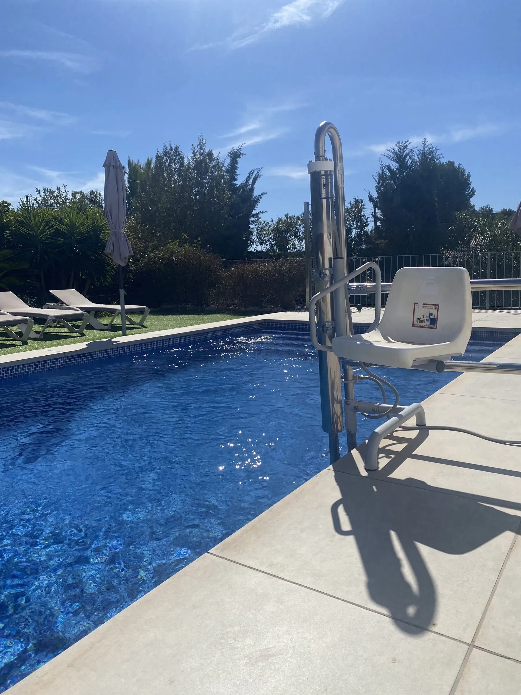 The hydraulic pool hoist with its seat, at the edge of the pool on level paving